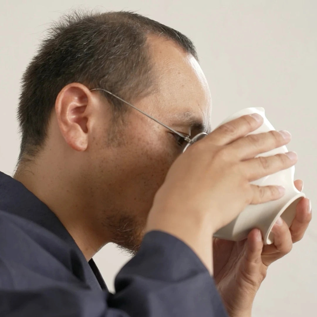 A man drinking from a white matcha bowl with a neutral background