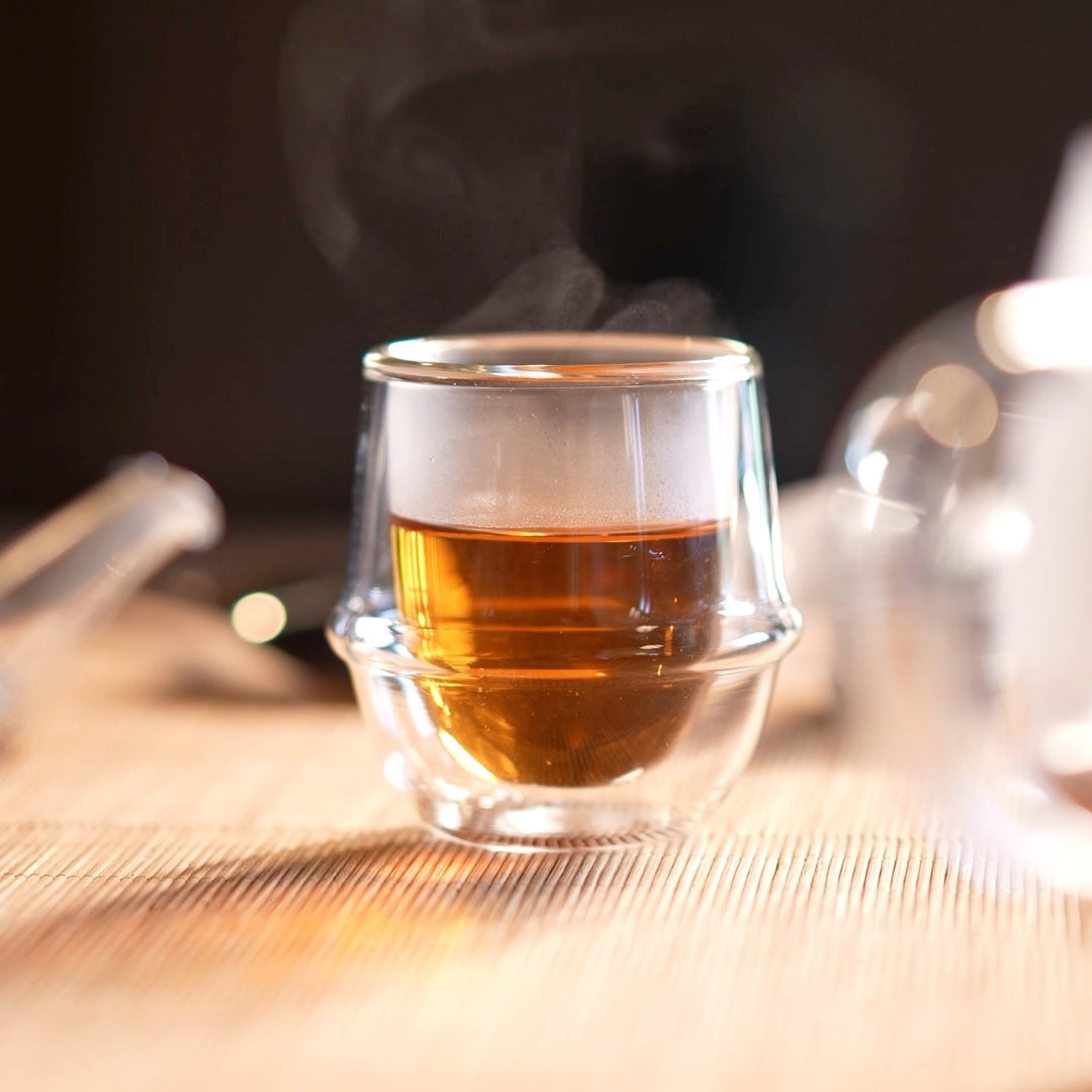 Steaming hot Japanese black tea in a clear glass cup on a wooden surface with a blurred background