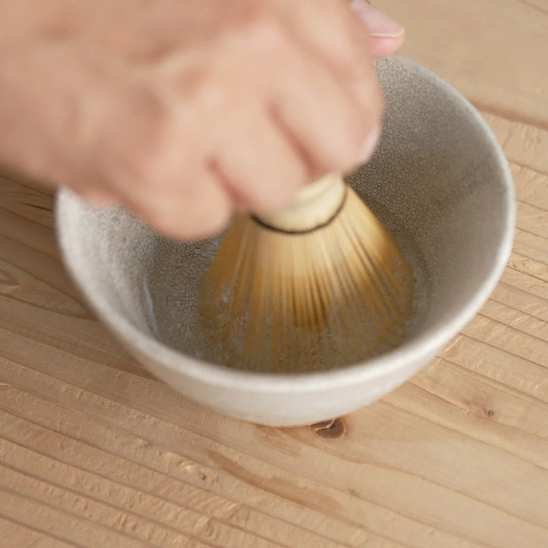 A person prepares a wooden tea whisk by putting it into hot water to soften it. 