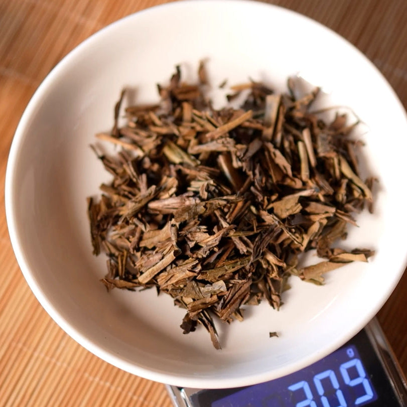Japanese roasted tea hojicha on a digital scale displaying weight, placed on a white plate.