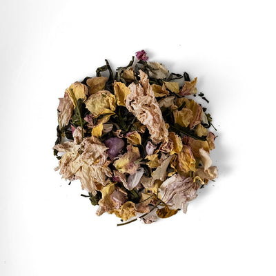 A pile of Kamairicha green tea leaves, cherry blossom petals, and peppermint on a white background